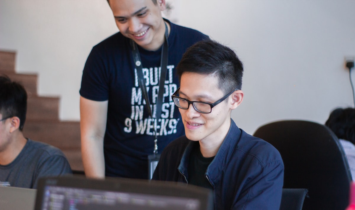 A mentor guiding a student at a laptop, representing schools teaching AI literacy by having students verify and question chatbot output
