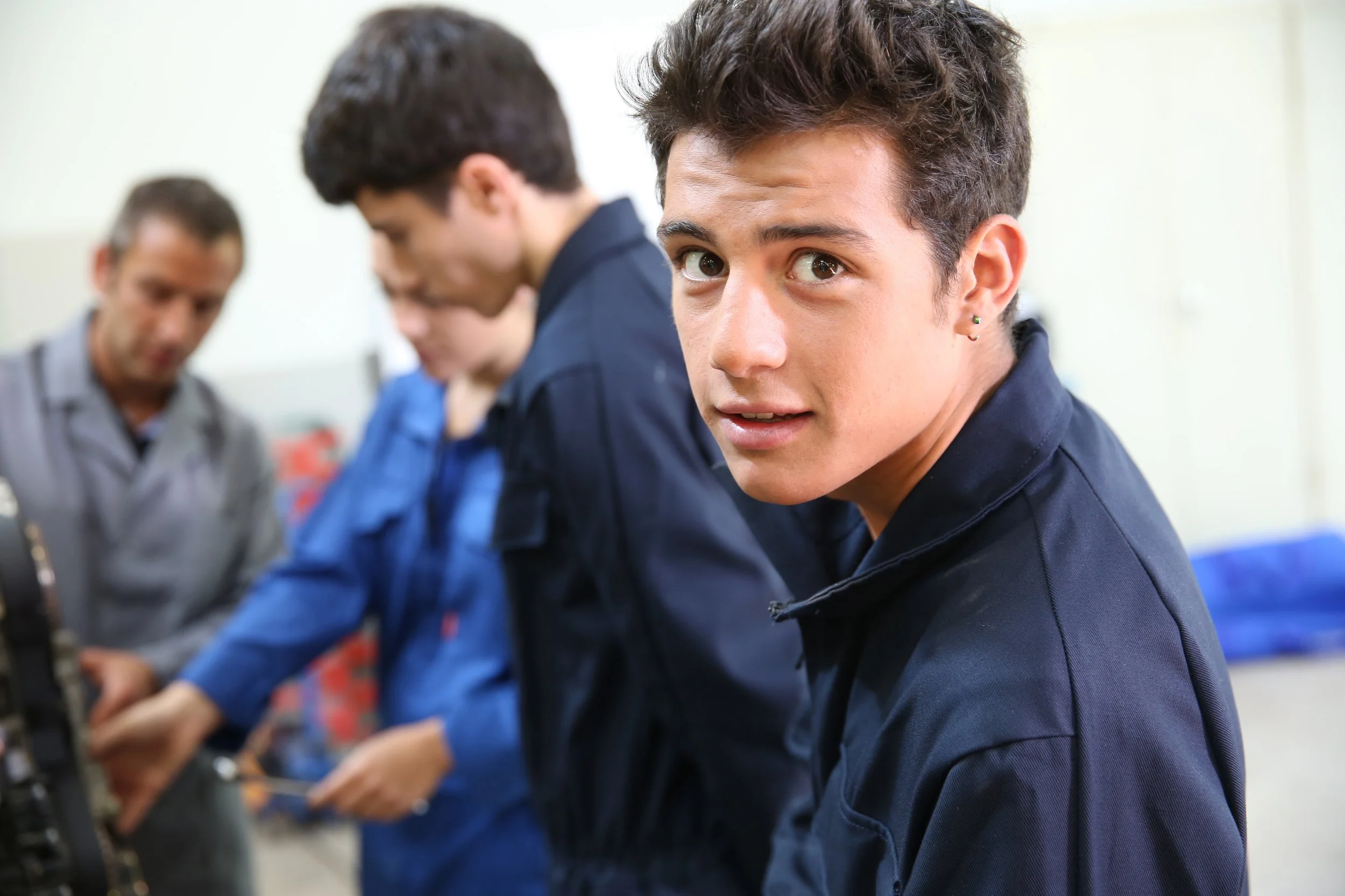 High school CTE students in coveralls working in an automotive shop, representing seniors preparing for industry credential exams